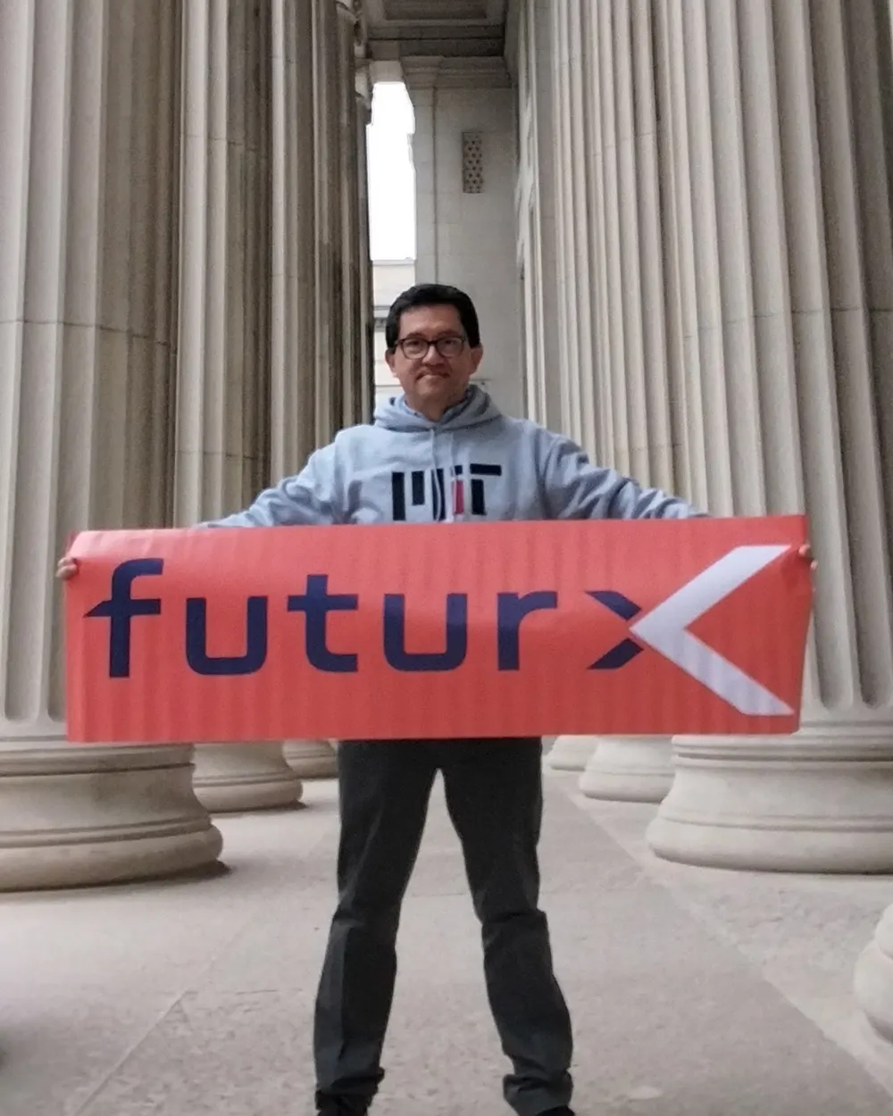 Un integrante sostiene la banderola de futurX frente a las columnas de un edificio universitario.